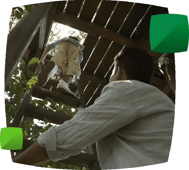 Boy climbing into treehouse whilst father watches